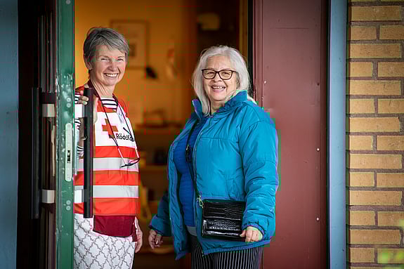 En kvinnlig volontär i Röda kors-väst öppnar dörren för en kvinnlig hjälpsökande i blå jacka.