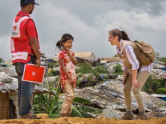 Flicka ler stort intill två vuxna volontärer i Bangladesh.