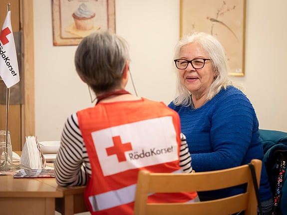 En kvinnlig volontär i Röda Kors-väst samtalar med en kvinnlig stödsökande i blå kofta.