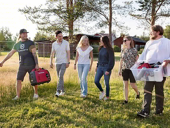 Personer bär på krislåda på en solig gräsmatta.