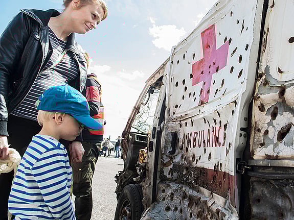 Mamma och barn tittar på skottskadad ambulans.