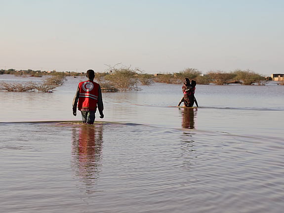 En syrisk röda korset-frivillig som springer genom rasmassor med en flicka i famnen. Det brinner i bakgrunden.