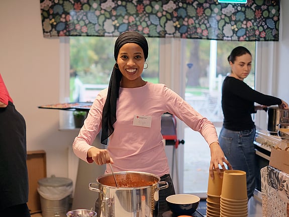 Ung kvinna serverar soppa ur stor kastrull.