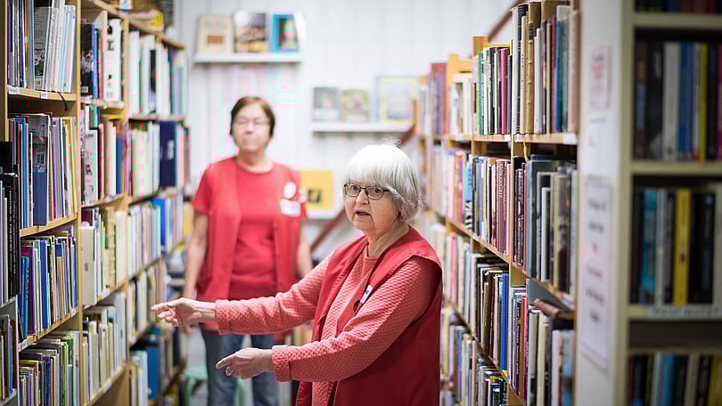 två-volontärer-står-vid-bokhyllor-fyllda-med-böcker-i-butiken