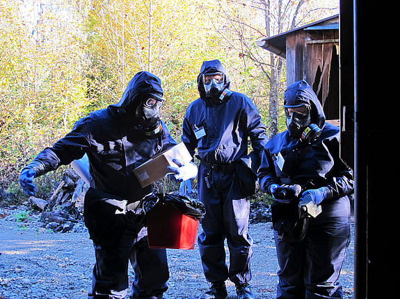 Tre personer i gasmasker och skyddskläder övar på hjälpinsatser där kemiska och biologiska vapen använts.