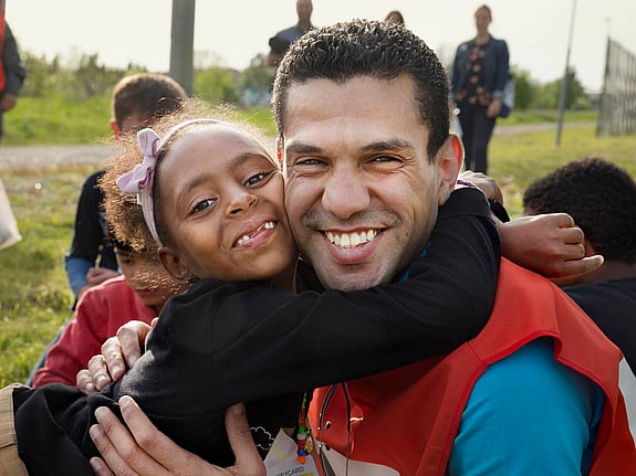En flicka ler och kramar om en rödakorsare.