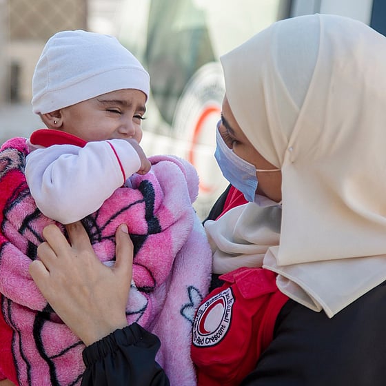 En liten flicka som håller i ett glas med te. I bakgrunden syns tält då hon befinner sig i ett flyktingläger.