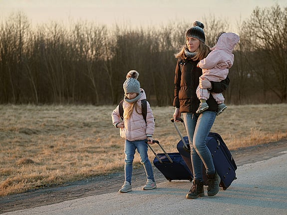 Mamma och barn går med resväskor på en väg