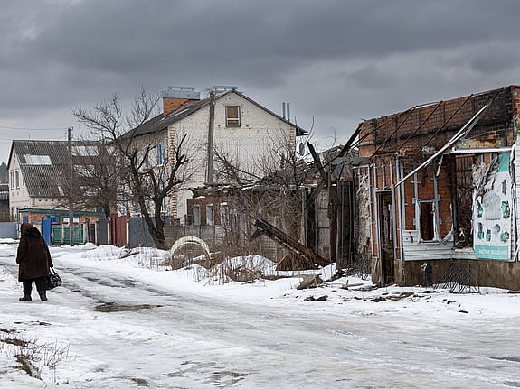 En gata i ett bostadsområde i Sumy i nordöstra Ukraina. Det är snö på marken och vädret är mulet. På gatan promenerar människor, ett av husen längs gatan är förstört efter en attack mot staden.