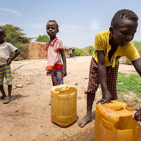 Barn hämtar vatten i gula vattendunkar.