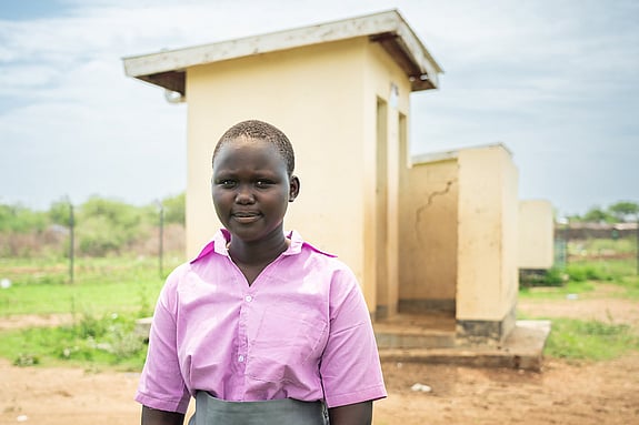Precious står framför en av utomhustoaletterna.