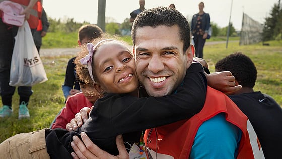 Ett barn kramar om en röda korsare och tittar in i kameran.