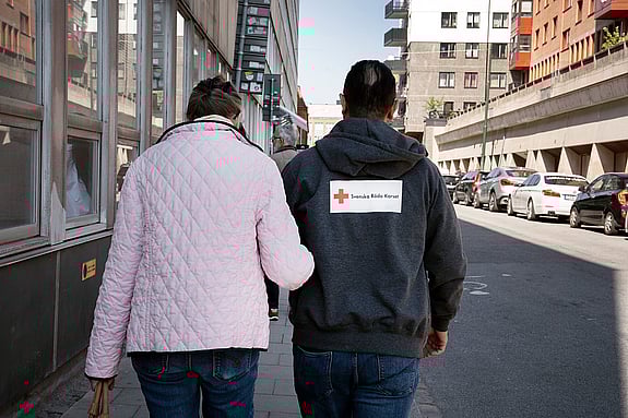 En senior går armkrok med en av Röda Korsets volontärer.