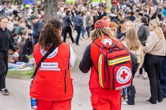 Två personer med rödakorsvästar står intill en folksamling under valborgsfirande