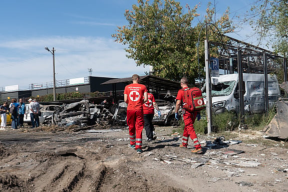 Bild på två jeepar med Röda Korset på som kör genom Gaza. Byggnaderna runt om kring har blivit drabbade av bomber och långt bort kan man se en byggnad med ett stort rött kors på sig.