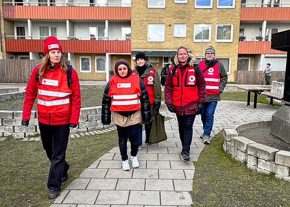 fem volontärer från Malmökretsens beredskapsgrupp är iklädda västar och går tillsammans över en gård utanför ett lägenhetshus.