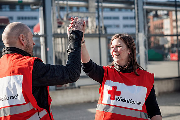 Två personer med rödakorsvästar ger varandra en high-five.