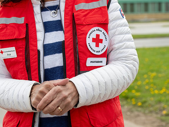 avbildar Röda Korset insatsledare, endast närbild på kvinnans överkropp, när hon har den röda västen på. Ansiktet syns ej. Hon håller sina händer knäppta framför kroppen.
