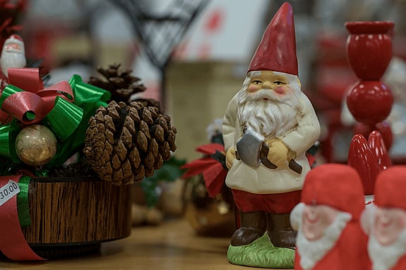 Juldekorationer på ett bord med en tomtefigur, kottar och röda prydnader.