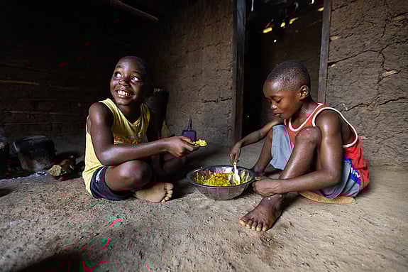 Richard The (i gult) och hans lillebror äter ris och palmgryta hemma i familjens kök, Podroken, Liberia. Efter att  Röda Korset utbildat om vikten av handtvätt och hygien har Richard varit friskare. ”Förut hade jag ofta ont i magen. Jag kräktes. Men nu är det inte så längre, för jag tvättar händerna när jag har varit på latrinen och innan jag äter.”