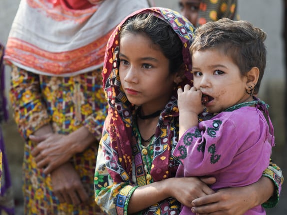 En liten flicka som håller i ett glas med te. I bakgrunden syns tält då hon befinner sig i ett flyktingläger.