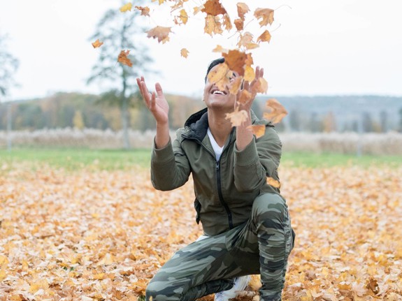 Pojke som kastar upp höstlöv i luften