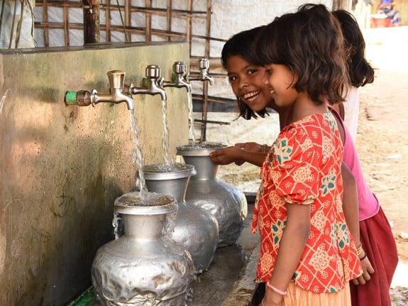 Tre flickor fyller på med vatten i flyktingläger.