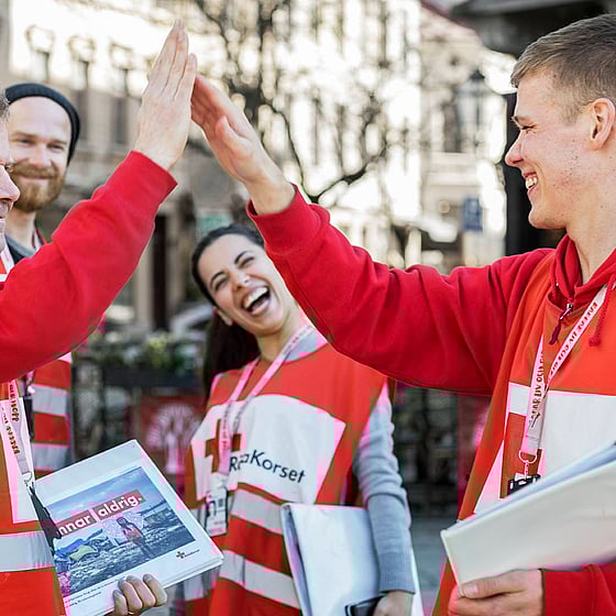 Glada värvare i Svenska Röda Korset-kläder gör en high five.