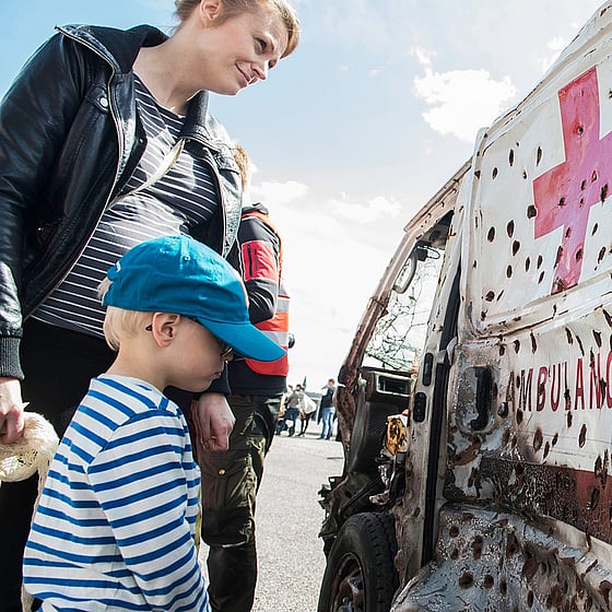 Mamma med barn tittar på skottskadad ambulans.