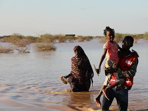 Röda kors-frivllig bär barn genom vatten.